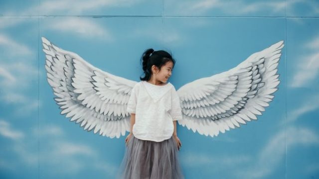 天使の羽が描かれた壁画の前に立つ女の子の画像