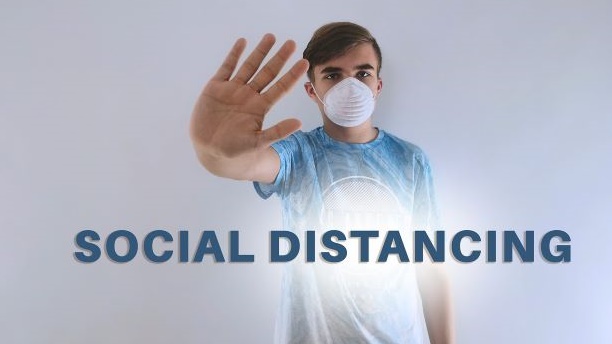 「social distancing 」の掲示板の前でストップのジェスチャーをするマスク姿の男性の画像