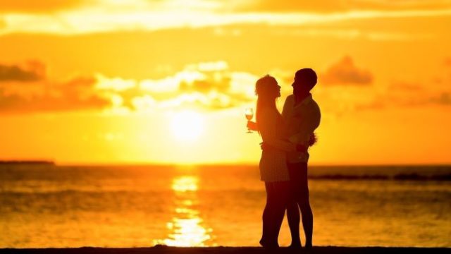 夕日が沈むビーチで寄り添うカップルの画像